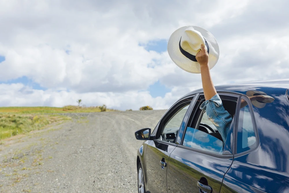 a person inside a car holding a hat outside the backseat side window